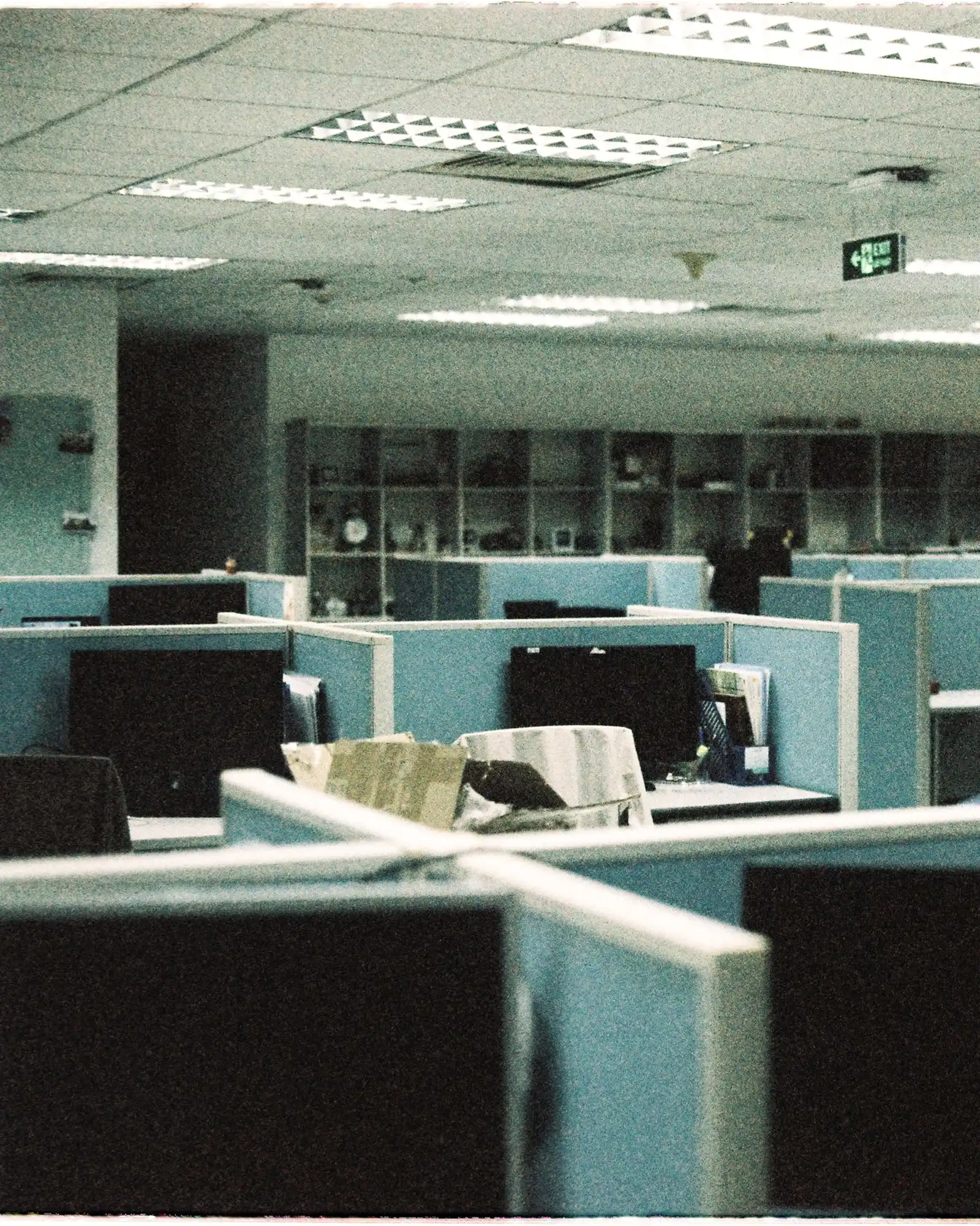 An empty office floor of desk cubicles with computer monitors, teal partition panels.