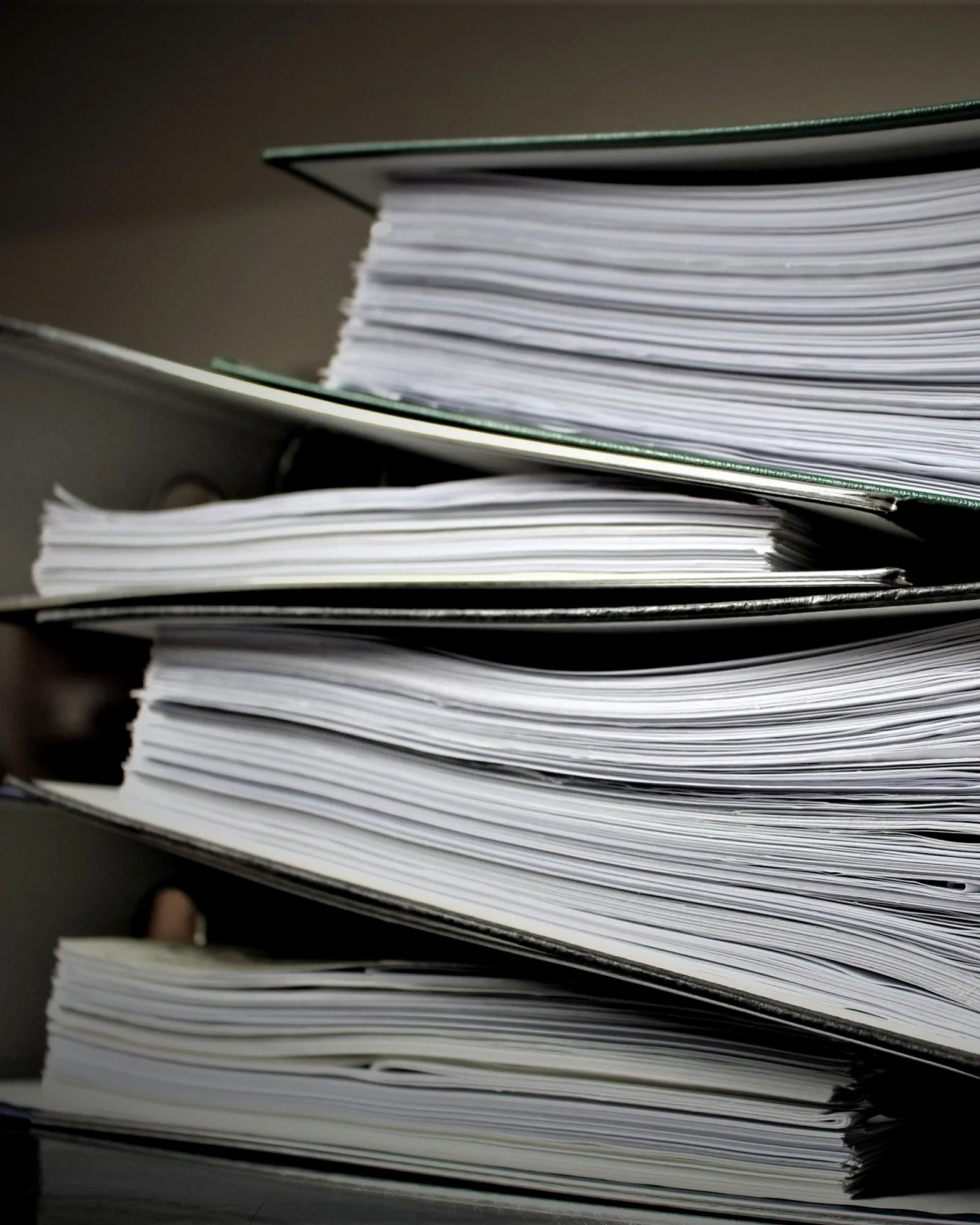 A stack of open ring binders filled with papers on an office shelf.
