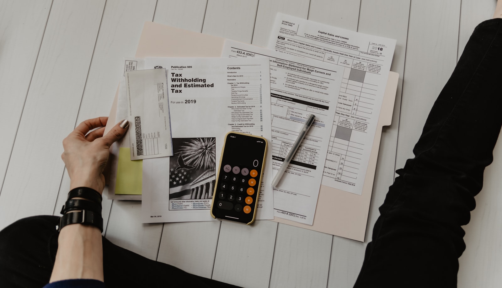 Flat-lay of hands with accounting documents, a folder, calculator, and pen
