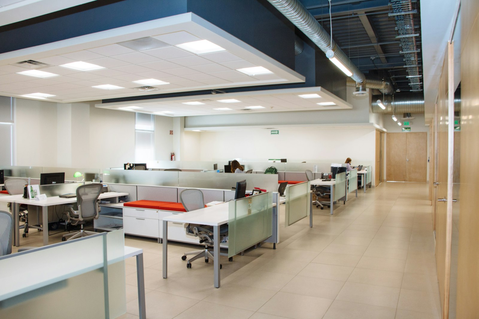 Clean open-plan office with white desks and glass-partition workstations, a few staff working at screens