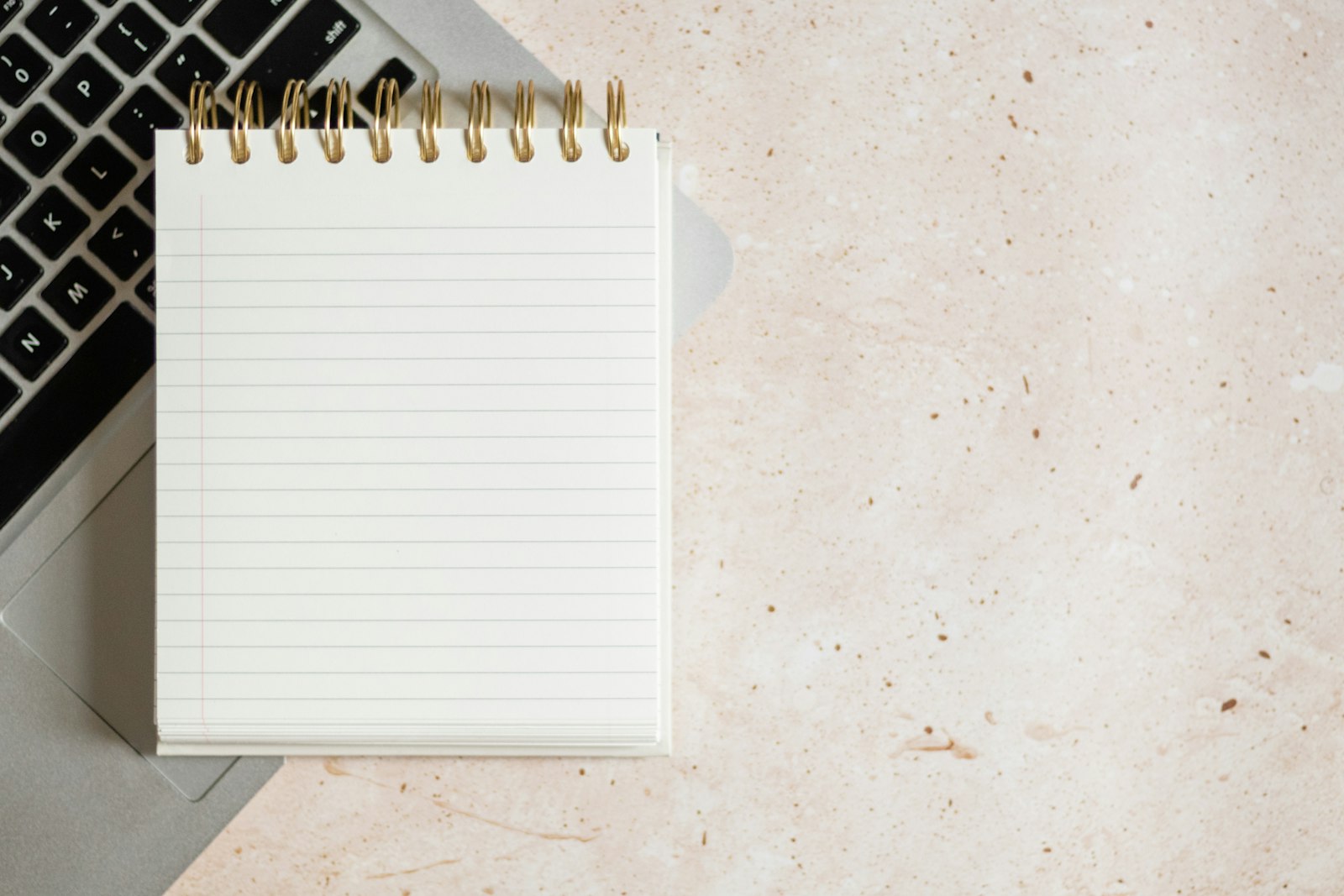 Calm flat-lay of a blank notepad resting on a laptop, on a neutral stone surface